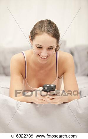Young woman using mobile phone on bed View Large Photo Image Stock Photography - Young woman using mobile phone on bed. Fotosearch