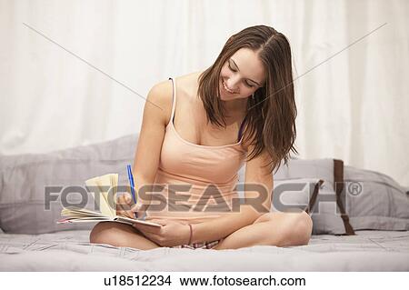 Picture - Young woman writing diary on bed. Fotosearch
