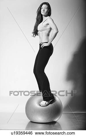 Stock Photograph - a woman in workout wear standing on an exercise ball; troutdale, oregon, united states of america. Fotosearch