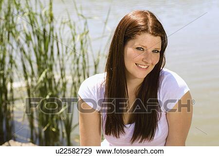 Stock Photo - portrait of a woman sitting by a lake; wilmar, minnesota, united states of america. Fotosearch