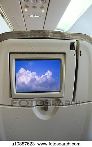Stock Image - Airplane seat with monitor displaying clouds. Fotosearch