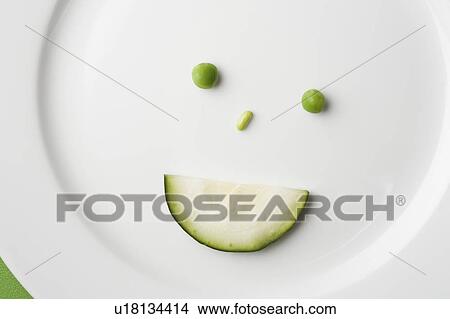 Picture - Anthropomorphic face made up from green peas and cucumber slice. Fotosearch