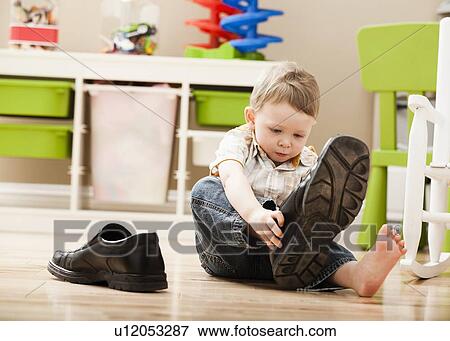Stock Photo - Boy (2-3) putting on dad's shoes. Fotosearch