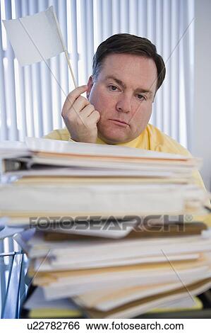 Stock Photograph - Businessman holding white flag over stack of paperwork. Fotosearch