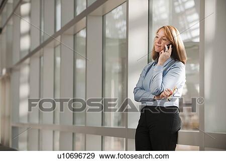 Stock Photo - Businesswoman talking on phone in corridor. Fotosearch