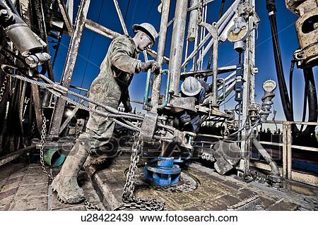 Stock Photo - Canada, Alberta, Oil workers using oil drill. Fotosearch