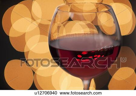 Stock Image - Close up of glass of red wine with defocused lights in background. Fotosearch