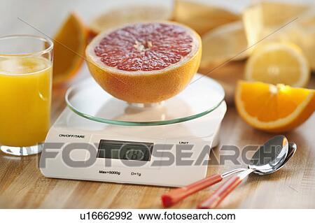 Stock Image - Close up of half of orange on kitchen scale. Fotosearch