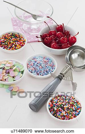 Stock Image - Close up of scoop and bowls with colorful toppings for ice creams. Fotosearch