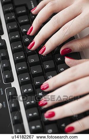 Stock Photo - Close up of woman's fingers with red nail polish typing on computer keyboard. Fotosearch