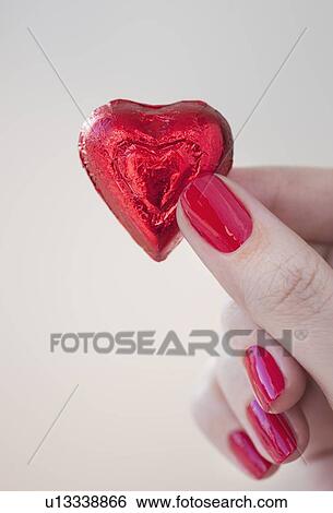 Close up of woman's fingers with red nail polish holding chocolate in shape of heart in red wrapping View Large Photo Image Stock Photograph - Close up of woman's fingers with red nail polish holding chocolate in shape of heart in red wrapping. Fotosearch