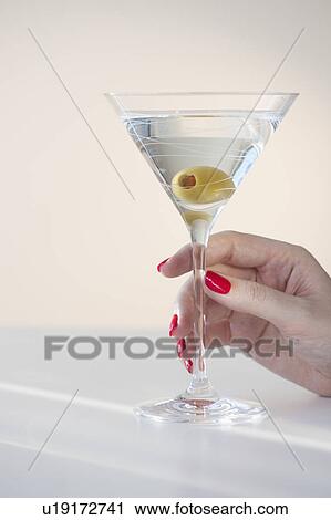 Stock Image - Close up of woman's hand with nail polish holding martini glass with olive. Fotosearch
