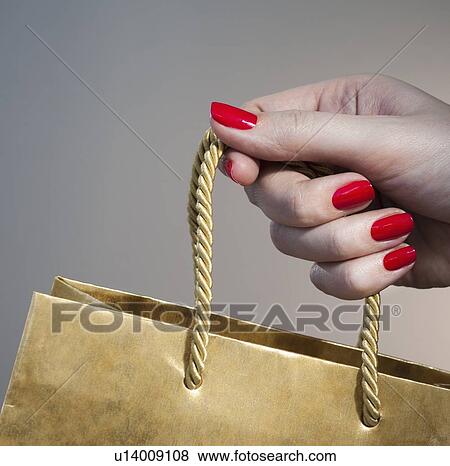 Stock Photo - Close up of woman's hand with red nail polish holding string handle of paper bag. Fotosearch