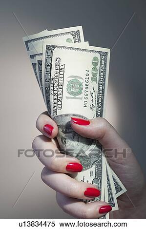 Stock Photography - Close up of woman's hand with red nail polish holding bunch of dollar banknotes. Fotosearch