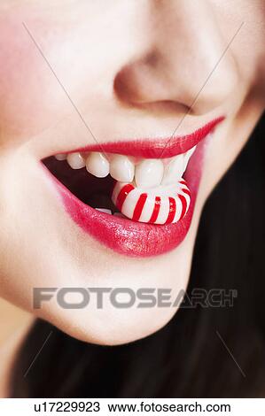 Stock Image - Close up of woman's mouths with red lipstick holding striped candy. Fotosearch