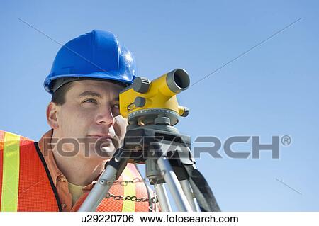 Stock Photograph - Construction worker in hard hat using theodolite. Fotosearch