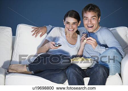 Stock Image - couple watching tv on sofa and eating popcorn. Fotosearch