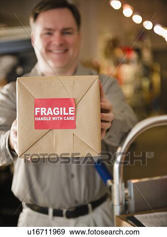 Delivery man holding box with fragile sign View Large Photo Image Stock Photo - Delivery man holding box with fragile sign. Fotosearch