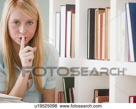 Stock Photo - Female student in library holding finger on lips. Fotosearch