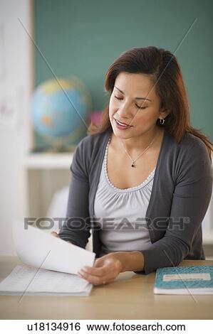 Female teacher sitting at desk in classroom View Large Photo Image Stock Photograph - Female teacher sitting at desk in classroom . Fotosearch