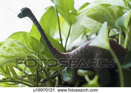 Stock Image - Figurine of dinosaur among leaves. Fotosearch