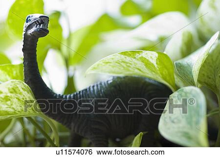 Stock Photograph - Figurine of dinosaur among leaves. Fotosearch