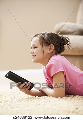 Stock Image - Girl (10-11) lying on floor holding remote control. Fotosearch