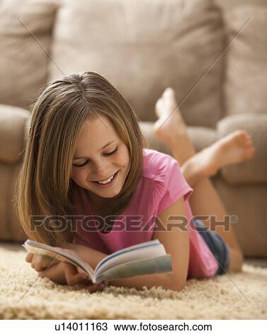 Stock Image - Girl (10-11) lying on rug, reading book. Fotosearch