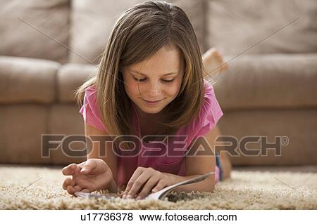 Stock Photo - Girl (10-11) lying on rug, reading book. Fotosearch