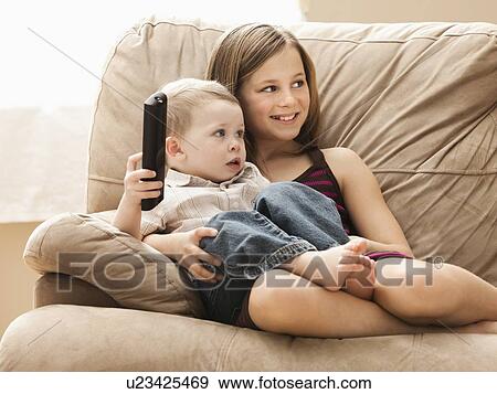 Girl (10-11) with brother (2-3) sitting on sofa, watching TV View Large Photo Image Stock Photo - Girl (10-11) with brother (2-3) sitting on sofa, watching TV. Fotosearch