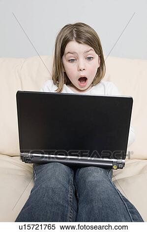 Stock Photography - Girl (6-7) with laptop sitting on sofa. Fotosearch