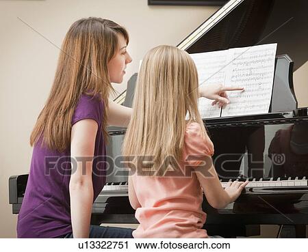Stock Image - Girl (8-9) and mother playing grand piano . Fotosearch