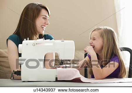 Stock Photo - Girl (8-9) and young woman using sewing machine. Fotosearch