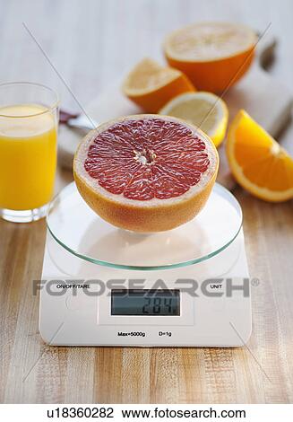 Stock Image - Half of grapefruit on weight scale. Fotosearch