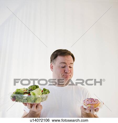 Stock Photograph - Man comparing donut and salad. Fotosearch