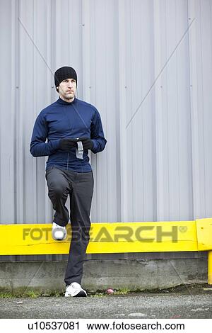 Stock Image - Man in sports clothing leaning against wall. Fotosearch