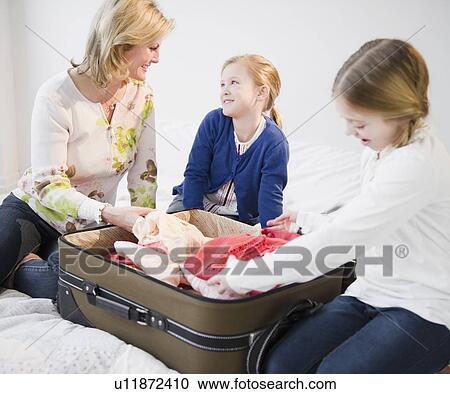 Stock Image - Mother and daughters (8-11) packing suitcase. Fotosearch
