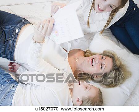 Stock Image - Mother and daughters (8-11) reading letter on bed. Fotosearch