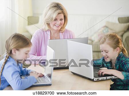 Stock Image - Mother and daughters (8-11) using laptop. Fotosearch
