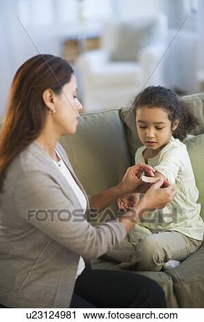 Stock Image - Mother applying bandaid on daughter's (6-7) arm . Fotosearch