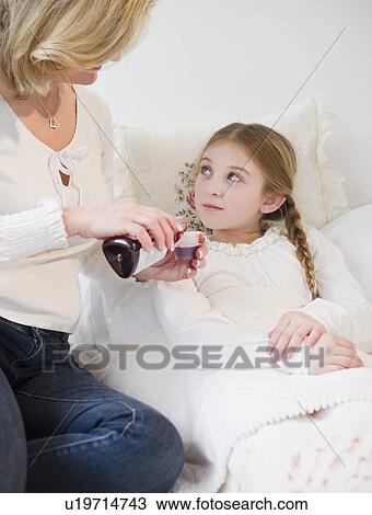 Stock Image - Mother giving medication to daughter (10-11) in bed. Fotosearch