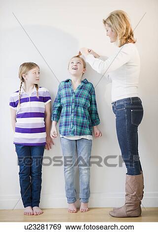 Stock Photo - Mother measuring daughters' (8-11) height. Fotosearch