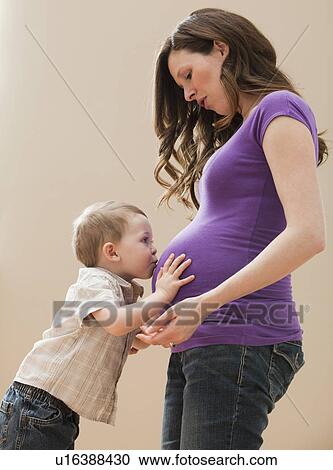 Stock Image - Portrait of boy (2-3) kissing pregnant mother's belly. Fotosearch