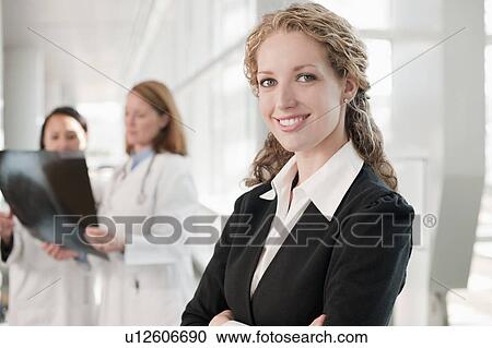 Stock Image - Portrait of businesswoman with doctors in background. Fotosearch