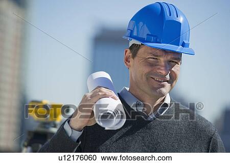 Stock Image - Portrait of construction worker holding rolled up blueprint. Fotosearch