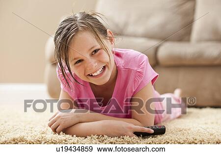 Stock Photo - Portrait of girl (10-11) lying on floor holding remote control. Fotosearch