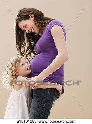 Stock Image - Portrait of girl (2-3) and pregnant mother embracing. Fotosearch