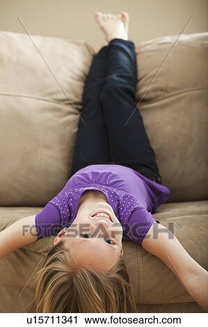 Stock Image - Portrait of girl (8-9) lying on sofa. Fotosearch