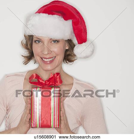Stock Image - Portrait of smiling woman in Santa hat holding gift. Fotosearch