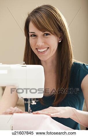 Stock Photography - Portrait of smiling young woman using sewing machine. Fotosearch